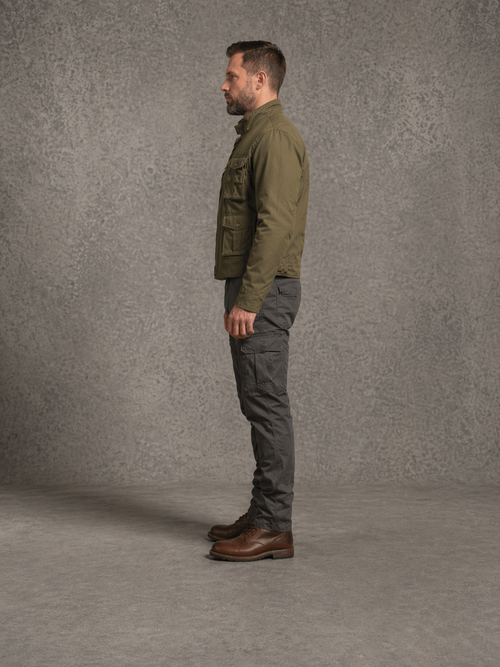 Man wearing a green jacket and gray pants standing against a gray background